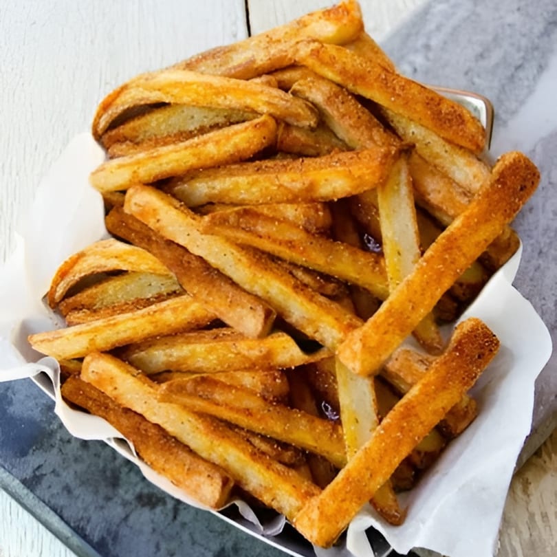 A close-up of golden-brown seasoned french fries in a white paper-lined basket from Cesar's Tacos.