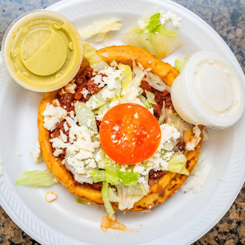 A Cesar's Tacos!!! gordita with chorizo, lettuce, cheese, and tomato, with two sauce containers.