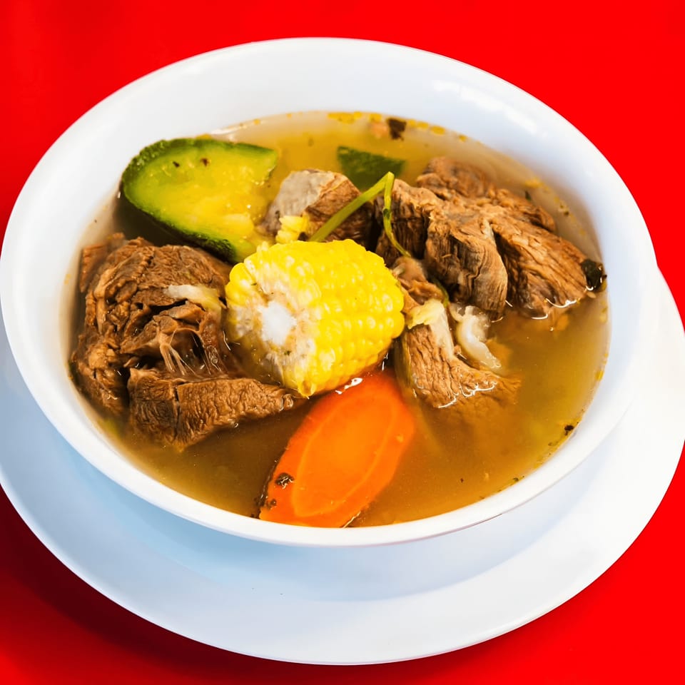 Hearty Mexican beef soup with corn, carrots, and avocado in a white bowl.