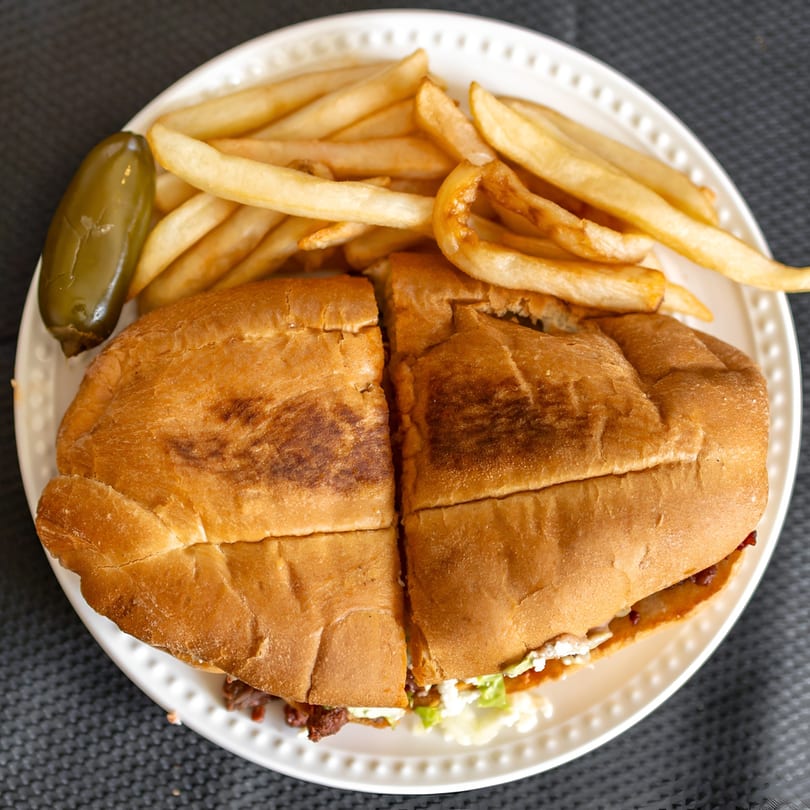 A Mexican torta sandwich, cut in half, with french fries and a pickled jalapeño on a white plate.