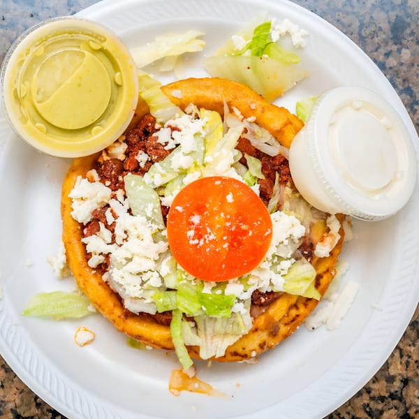 A Mexican sopes dish with meat, lettuce, cheese, and tomato, served with two sauces.